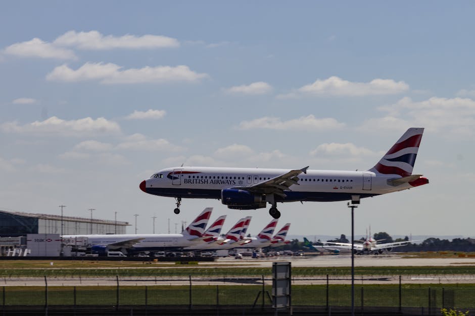 A British Airways commercial airplane with a white fuselage, blue underbelly, and red, white, and blue livery on the tail fin, is captured mid-air while performing a landing approach above an airport